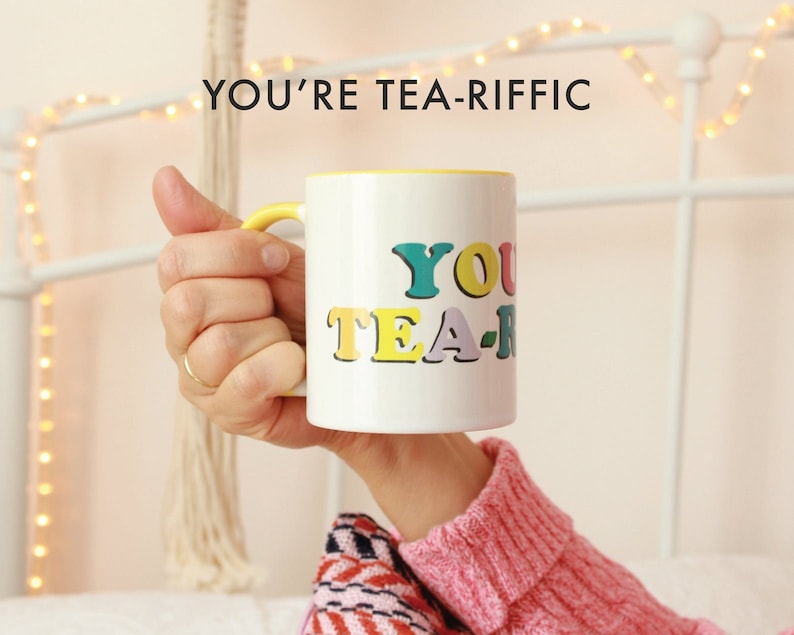 May include: White ceramic mug with a yellow rim and handle. The mug has the text "YOU'RE TEA-RIFFIC" in colorful letters.