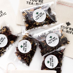 May include: Five small clear bags filled with loose leaf tea blends. Each bag has a round white sticker with the text "You're Tea-Rific" and a small green teapot icon. The bags are on a white surface.