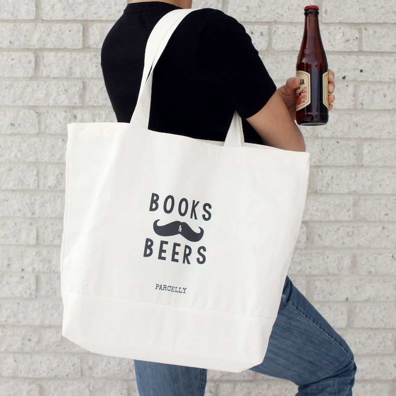 Może przedstawiać: Biała torba z pł&oacute;tna z czarnym tekstem, kt&oacute;ry brzmi "BOOKS & BEERS" z czarnym wzorem wąs&oacute;w i słowem "PARCELLY" poniżej.