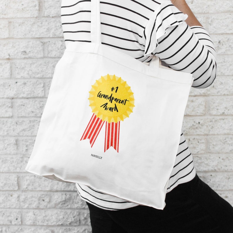 May include: White tote bag with a yellow and red graphic of a #1 Grandparent Award ribbon. The text "PARCELLX" is printed in the bottom left corner.