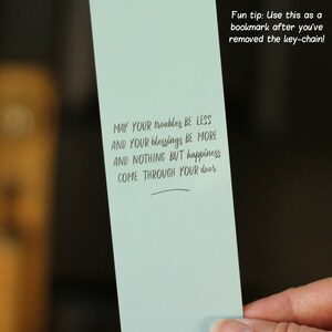 May include: A light blue bookmark with the text "MAY YOUR troubles BE LESS AND YOUR blessings BE MORE AND NOTHING BUT happiness COME THROUGH YOUR door" and the text "Fun tip: Use this as a bookmark after you've removed the key-chain!"