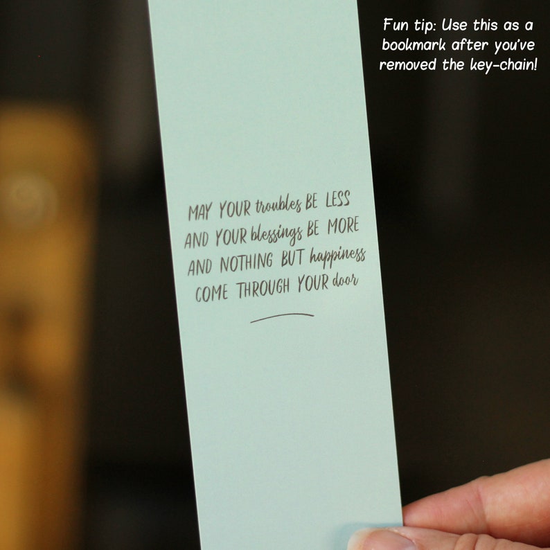 May include: A light blue bookmark with the text "MAY YOUR troubles BE LESS AND YOUR blessings BE MORE AND NOTHING BUT happiness COME THROUGH YOUR door" and the text "Fun tip: Use this as a bookmark after you've removed the key-chain!"