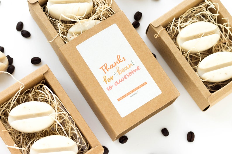 May include: A set of four small brown boxes with lids, each containing two white coffee bean-shaped soaps. The boxes are filled with shredded brown paper. One box has a sticker that says "Thanks for bean so awesome".