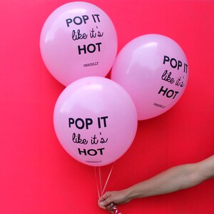 May include: Three pink balloons with the text "POP IT like it's HOT" printed on them. The balloons are tied together with a white ribbon.