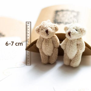 May include: Two small, beige teddy bears, each measuring 6-7 cm tall, are sitting on a brown paper bag. The bears have brown eyes and noses.