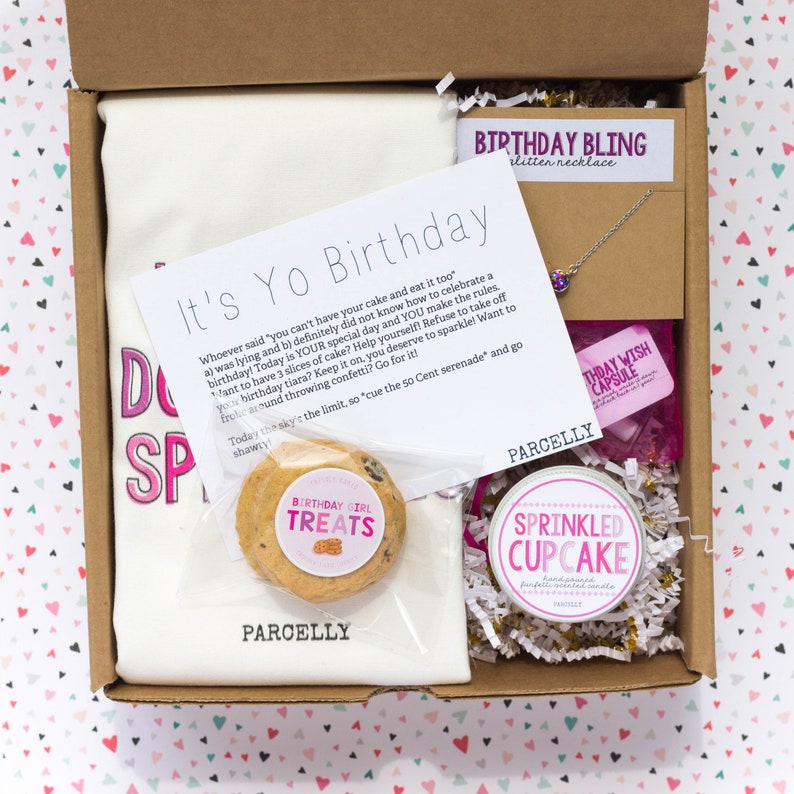 May include: A birthday gift box with a white t-shirt that says "It's Yo Birthday" in pink letters, a cookie, a small jar of cupcake frosting, a birthday wish capsule, a silver necklace with a purple gem, and a note that says "Whoever said 'you can't have your cake and eat it too' was lying and b) definitely did not know how to celebrate a birthday! Today is YOUR special day and YOU make the rules. Want to have 3 slices of cake? Help yourself! Refuse to take off your birthday tiara? Keep it on, you deserve to sparkle! Want to frolic around throwing confetti? Go for it! Today the sky's the limit, so "cue the 50 Cent serenade" and go shawty!"
