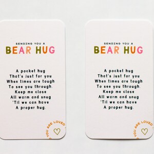 May include: Two white cards with colourful text that reads "Sending you a Bear Hug". The cards have a poem about a hug and a heart with the text "You are Loved" in a circle.