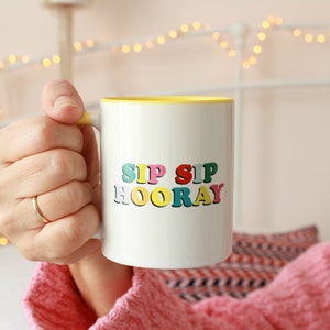 May include: White ceramic mug with a yellow rim and the text "SIP SIP HOORAY" in colorful letters.