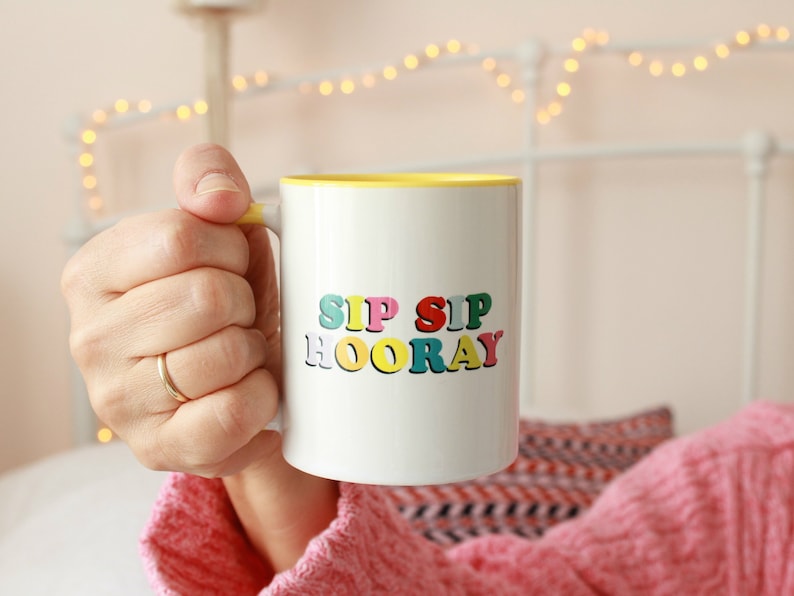 May include: White ceramic mug with a yellow rim and the text "SIP SIP HOORAY" in colorful letters.