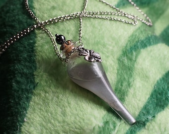 May include: A silver teardrop-shaped glass bottle pendant necklace with a cork stopper, a silver butterfly charm, and a silver chain. The bottle is filled with a silver glitter-like substance.