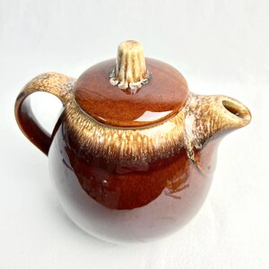 May include: A vintage brown ceramic teapot with a lid and handle. The teapot has a glossy finish with a two-tone colour scheme, transitioning from a dark brown base to a lighter, speckled rim. The lid features a decorative knob.