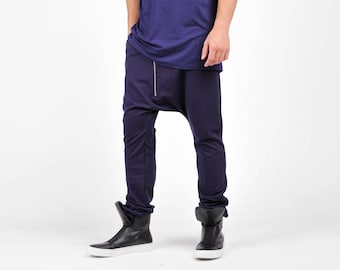May include: A man wearing a navy blue long-sleeved shirt and navy blue trousers with a zip detail. He is wearing black high-top trainers.