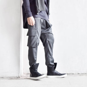 Puede incluir: Un hombre con una camisa negra de manga larga, una bufanda gris, pantalones cargo grises y zapatillas negras de caña alta.