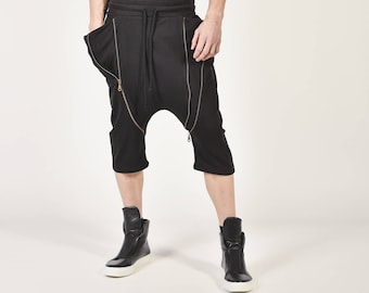 Op de afbeelding: Een man draagt een zwart tanktop en een zwarte broek met ritsdetails. Hij draagt zwarte high-top sneakers.