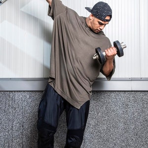May include: A man wearing a black cap, a green t-shirt, black pants, and black sneakers is lifting a dumbbell with his right arm.