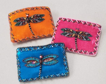 May include: Three small velvet pillows with beaded dragonfly designs. The pillows are orange, pink, and blue.