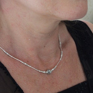 May include: A silver necklace with a small, round pendant featuring a black, intricate design. The necklace is worn by a person with a black top.