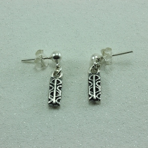Peut inclure: Une paire de boucles d'oreilles pendantes en argent avec un motif géométrique. Les boucles d'oreilles ont une petite boule en haut et un pendentif rectangulaire long avec un motif détaillé.