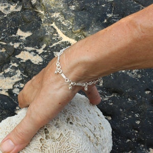 May include: A silver chain bracelet with small silver beads dangling from it. The bracelet is on a person's wrist.