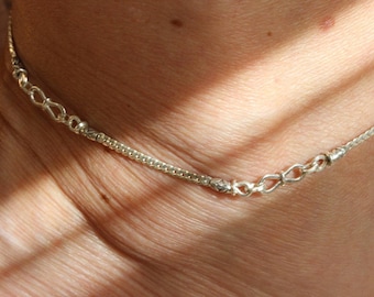 Puede incluir: Un tobillo de cadena de plata con un cierre decorativo. El tobillo está hecho de una cadena fina y delicada y tiene un diseño simple.