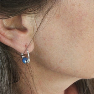 Puede incluir: Un arete de aro plateado con un dije de cuentas azules.