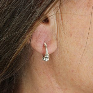 Peut inclure: Boucles d'oreilles créoles en argent avec un design empilé. Les boucles d'oreilles sont portées à l'oreille d'une personne.