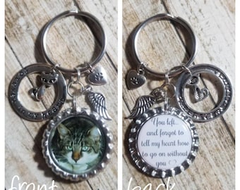 May include: A silver keychain with a photo of a tabby cat, a charm with a paw print, a charm with wings, and a charm with the text "Forever in my heart". The back of the keychain has a charm with the text "You left... and forgot to tell my heart how to go on without you".