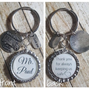 May include: Silver keyring with a round charm that says "Mr. Paul" and a charm with a school bus and the words "Awesome Bus Driver". The back of the keyring has a charm that says "Thank you for always keeping us safe" with a heart.