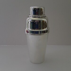 May include: A polished silver cocktail shaker. The shaker is made up of three parts: a top cap, a mid-section, and a base. The design is classic and the metal is highly reflective, suitable for mixing drinks.