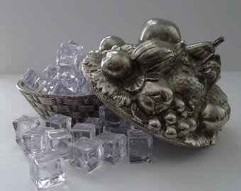 Puede incluir: Una cesta de frutas de metal plateado con un diseño detallado de frutas en la tapa. La cesta está llena de cubitos de hielo transparentes, con algunos cubitos que se derraman. La cesta está hecha de metal tejido.