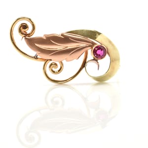 May include: A gold and rose gold brooch with a leaf design and a single red gemstone.