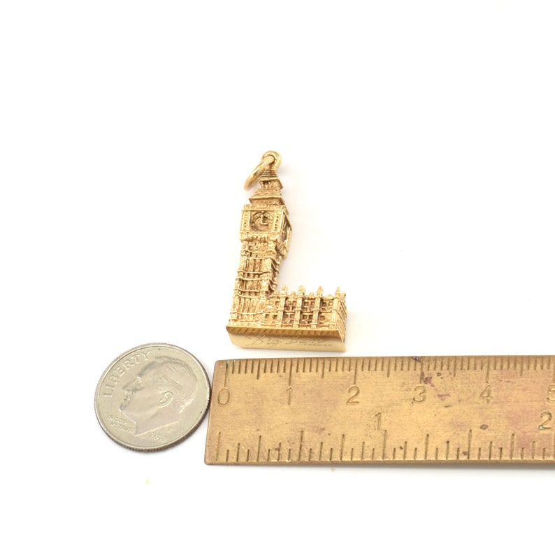 May include: Gold-colored charm of Big Ben, the famous clock tower in London, England. The charm is about 1.5 inches tall and is made of metal. It is a detailed replica of the iconic landmark.