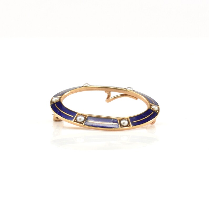 May include: An oval-shaped brooch with a blue enamel design and a border of small white pearls.