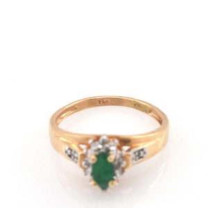 May include: A gold ring featuring a central marquise-cut green gemstone surrounded by a halo of small clear stones. The band is polished gold and includes a clear 14K stamp on the inner surface, indicating the metal purity of the jewelry piece.