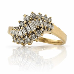 May include: A gold ring featuring a cluster of diamonds. The ring has a unique design with a mix of round and baguette-cut diamonds. The diamonds are set in a gold band, creating a sparkling and elegant piece of jewelry.