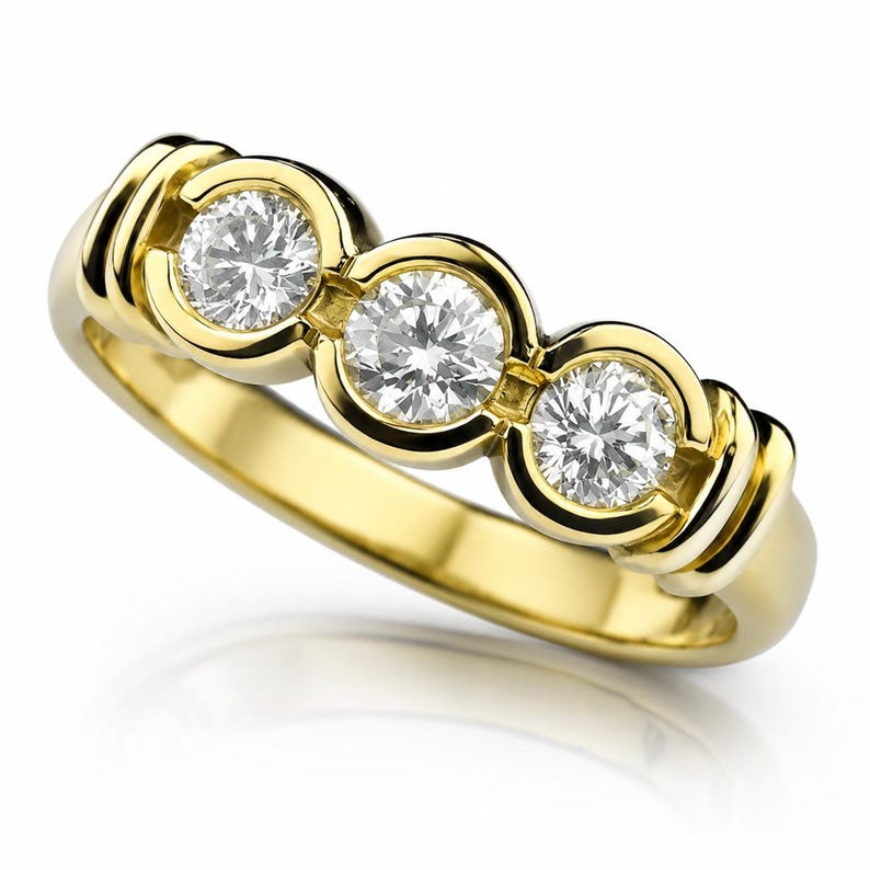 May include: A yellow gold ring featuring three round brilliant-cut white diamonds set in a horizontal row. Each diamond is secured within a smooth, circular bezel setting that is integrated into the polished gold band of the ring.