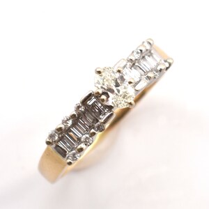 May include: A gold and silver ring with multiple diamonds. The ring features a central cluster of oval-cut diamonds and baguette-cut diamonds set along the band. The ring is set against a white background.
