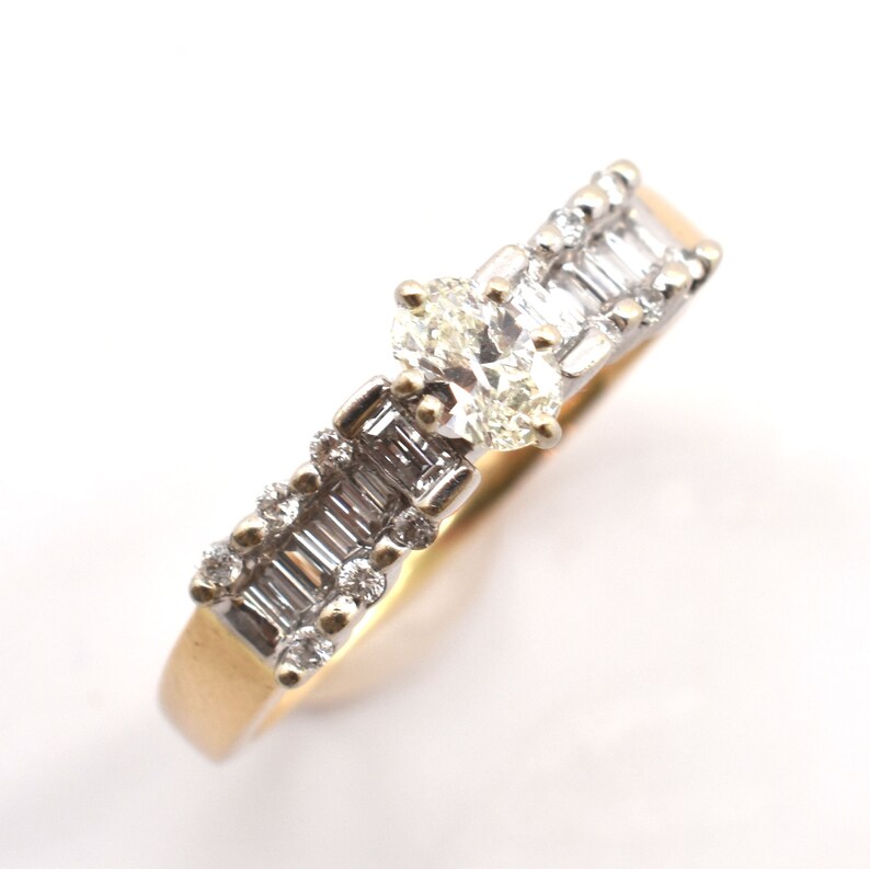May include: A gold and silver ring with multiple diamonds. The ring features a central cluster of oval-cut diamonds and baguette-cut diamonds set along the band. The ring is set against a white background.