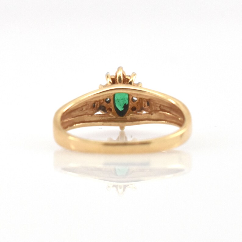 May include: A gold ring featuring a central marquise-cut green gemstone. The band is smooth and polished, with a setting that holds the stone securely. The design includes small, clear accent stones surrounding the main green gem.