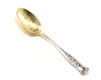 May include: A silver spoon with a gold-plated bowl. The bowl is engraved with the word "Congratulations". The handle is decorated with a floral pattern.