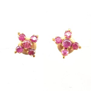 Può includere: Un paio di orecchini a bottone in oro con pietre di rubino rosa incastonate a forma di stella.