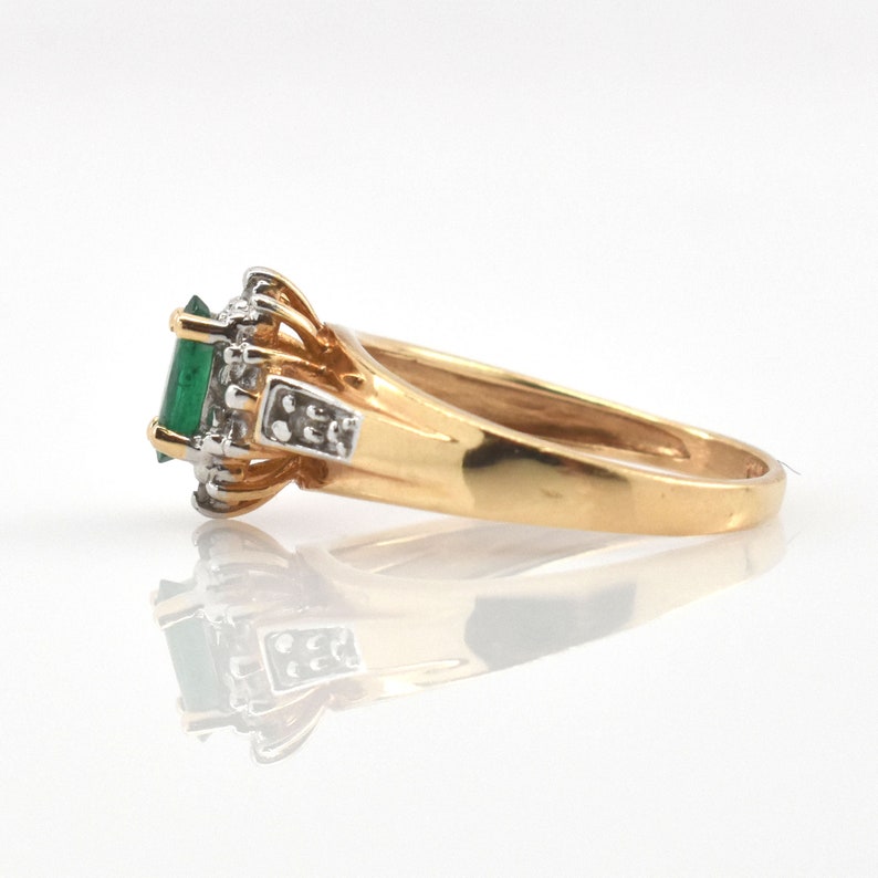 May include: A gold ring featuring a central rectangular green gemstone set in a white metal prong setting. The band is polished yellow gold, and the setting is accented with small clear stones on the sides, creating a multi-toned metal appearance.