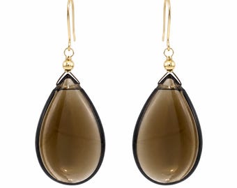 May include: A pair of teardrop-shaped earrings featuring translucent, smoky brown gemstones. Each gemstone is encased in a thin, dark frame and suspended from a gold-toned metal hook by a small, polished gold-toned bead connector.