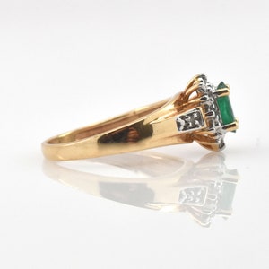May include: A gold ring featuring a central emerald-cut green gemstone surrounded by a halo of small white diamonds. The setting is crafted from yellow gold with white gold accents near the stone, showcasing a polished band and side details.