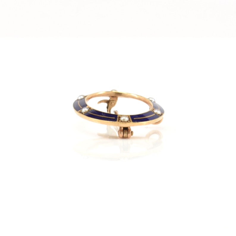 May include: A gold-toned circular brooch with a blue enamel design and white pearl accents.