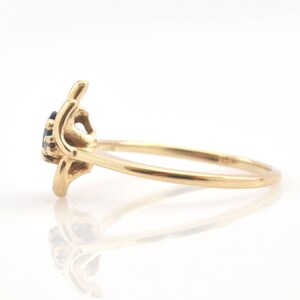 May include: A gold ring featuring a dark blue gemstone set in a prong setting. The band is smooth and polished, with a side profile view showing the elevated mounting of the stone and the curved metal structure that holds the gem securely in place.