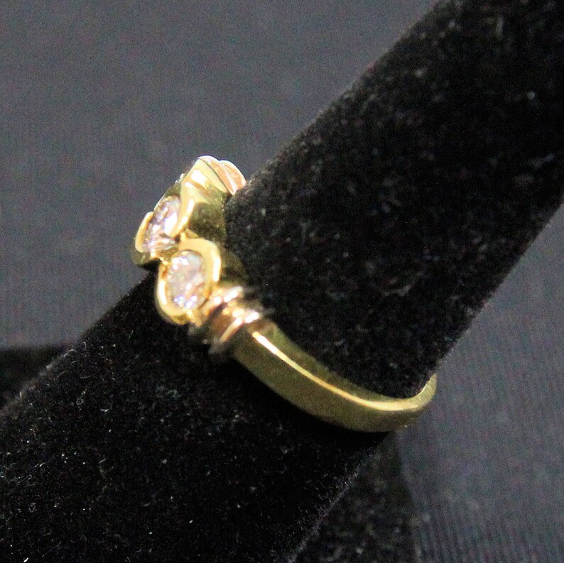 May include: A gold ring featuring a series of three round, clear, faceted stones set in a row. The band is crafted from polished yellow gold, and the stones are held in place by individual metal settings that follow the curve of the ring.