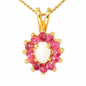 May include: A gold pendant necklace featuring a central oval white cabochon stone surrounded by a halo of twelve round faceted pink rubies. The pendant is suspended from a delicate gold chain, showcasing a classic floral-inspired cluster design.