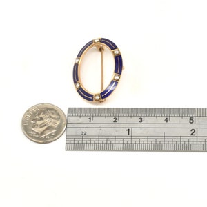 May include: A gold oval brooch with blue enamel and white pearl accents. The brooch is approximately 1 inch in diameter.