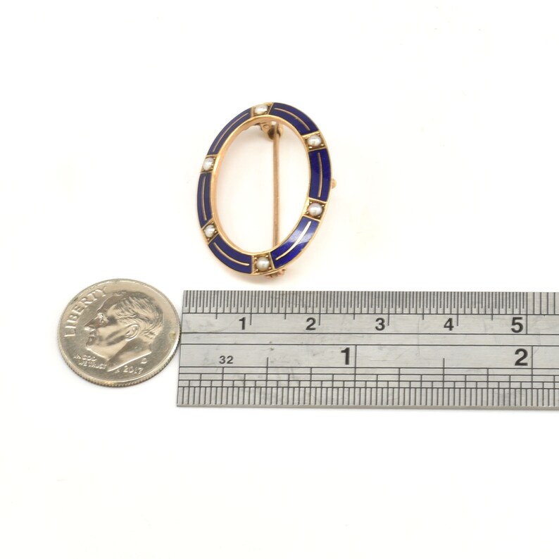 May include: A gold oval brooch with blue enamel and white pearl accents. The brooch is approximately 1 inch in diameter.